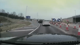 A line of cars are driving along a slip road with roadworks clearly visible to the side