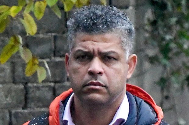 a man wearing an orange rab jacket stands in front of a brick wall