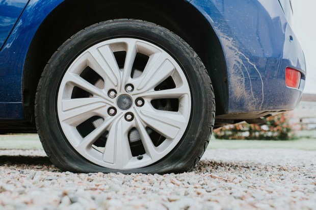 a blue car with a flat tire on gravel