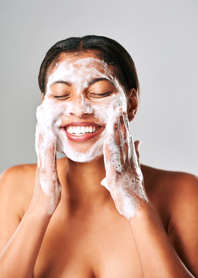 a woman is smiling while washing her face with soap