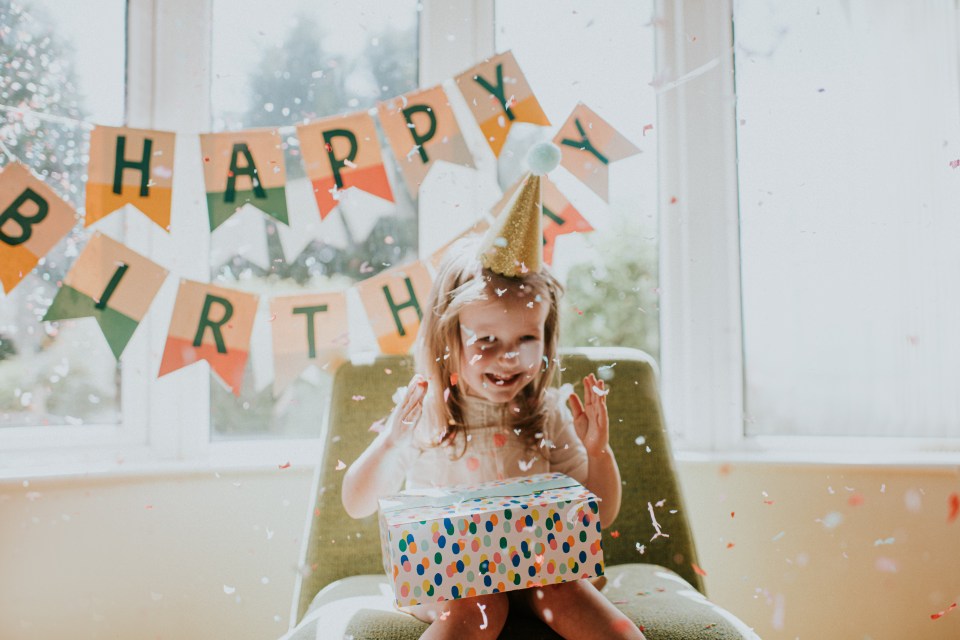 a little girl is holding a birthday present in front of a happy birthday banner