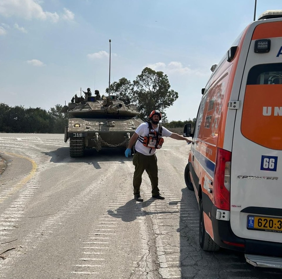 Chezi standing in front of an IDF tank alongside a United Hatzalah ambulance