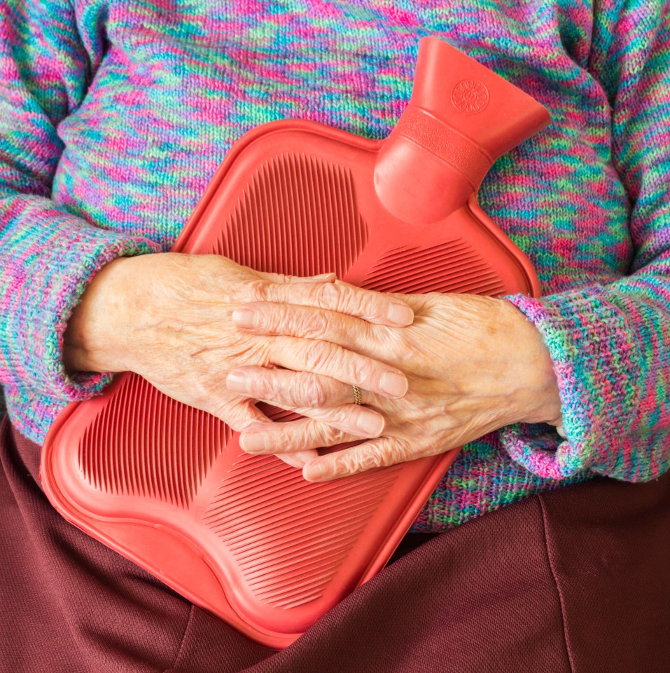 an elderly woman holds a red hot water bottle on her stomach