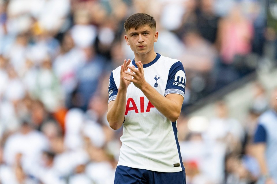 a young man wearing a tottenham shirt stands in the rain