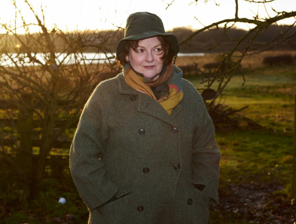 a woman in a green coat and hat stands in a field