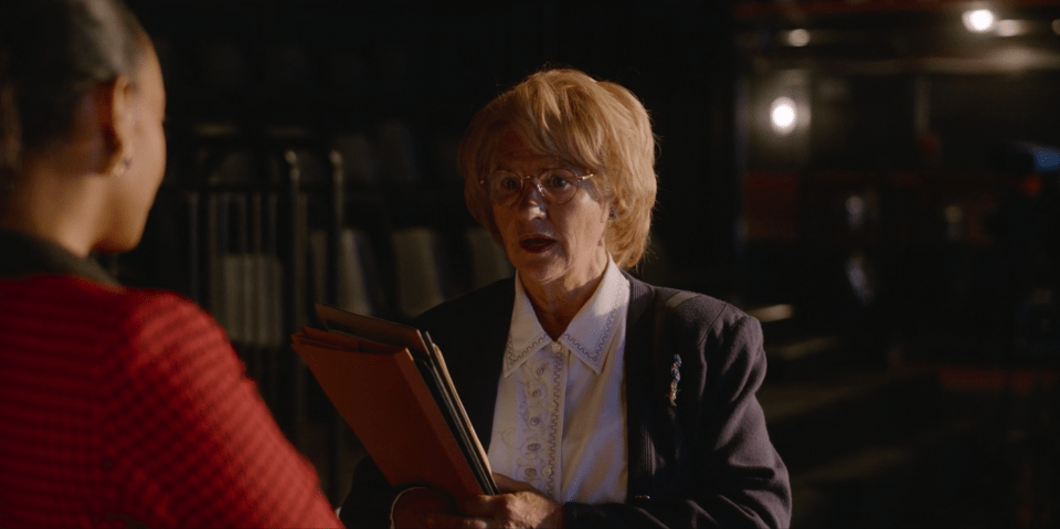 a woman with glasses is holding a folder and talking to another woman