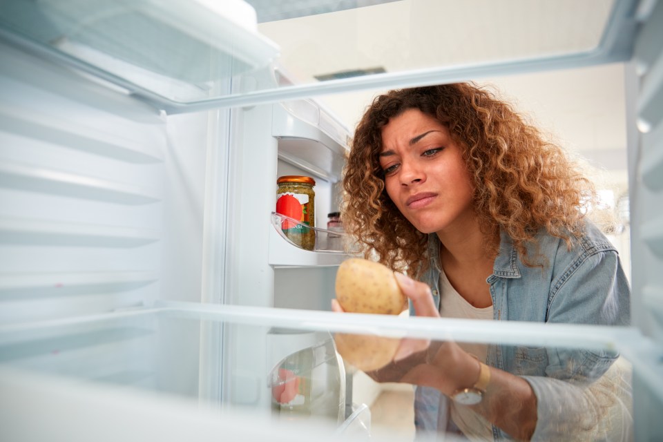 a woman takes a potato out of an open refrigerator