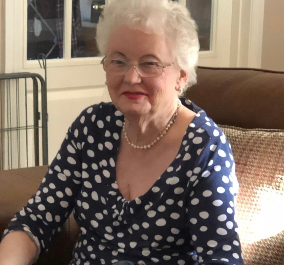 an elderly woman wearing a blue and white polka dot shirt sits on a couch