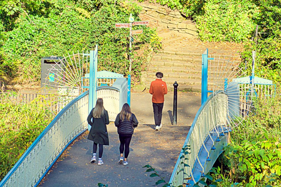 a man and two women walk across a bridge with a sign that says ' kings park ' on it