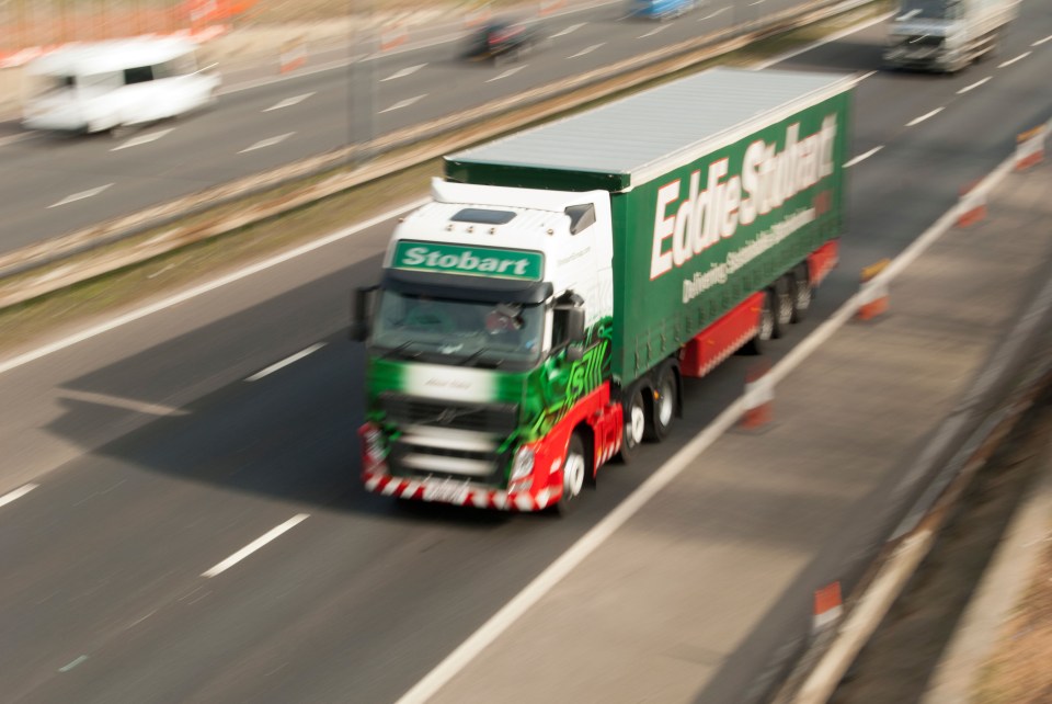 a green and white stobart truck is driving down a highway