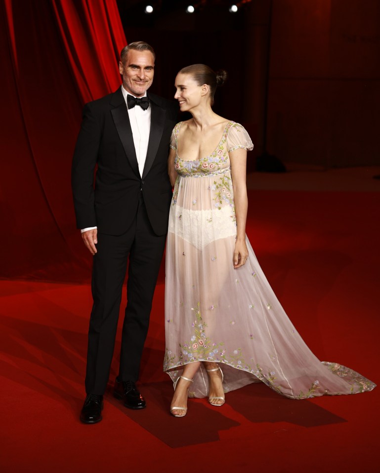 a man in a tuxedo stands next to a woman in a sheer dress