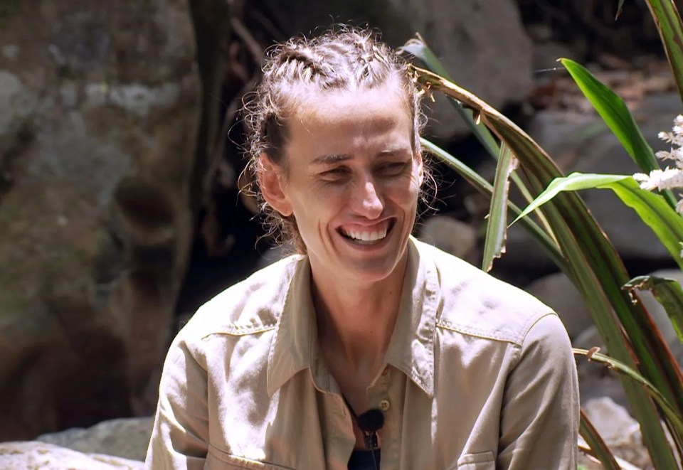 a woman in a tan shirt is smiling in front of some plants