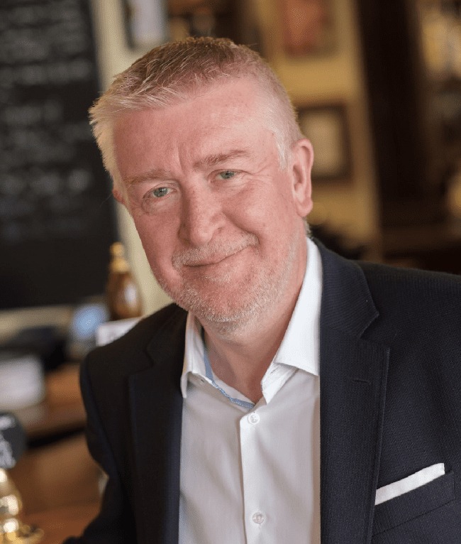 a man in a suit and white shirt smiles for the camera