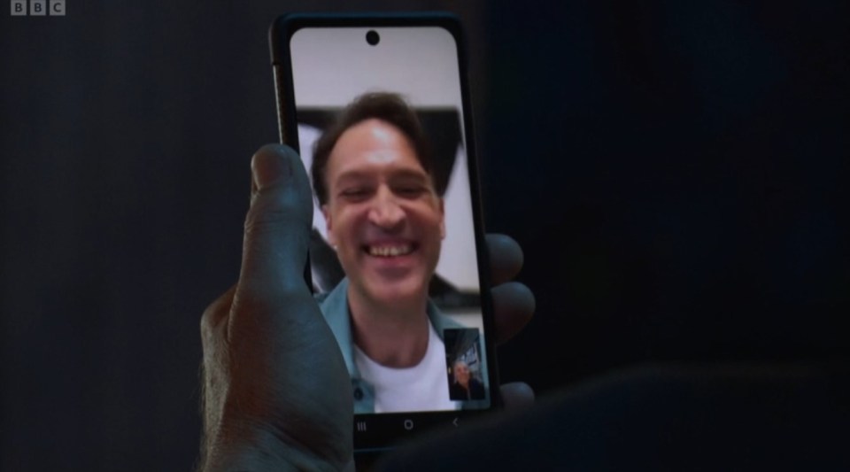 a person is holding a cell phone with a picture of a smiling man on it