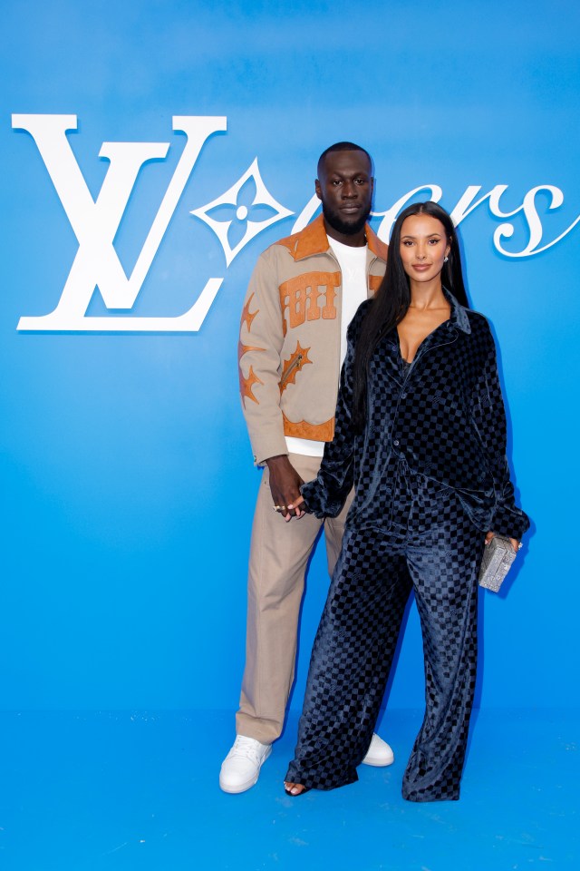 a man and a woman pose in front of a large louis vuitton logo