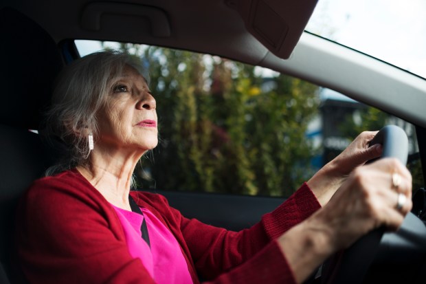 an older woman in a red sweater is driving a car