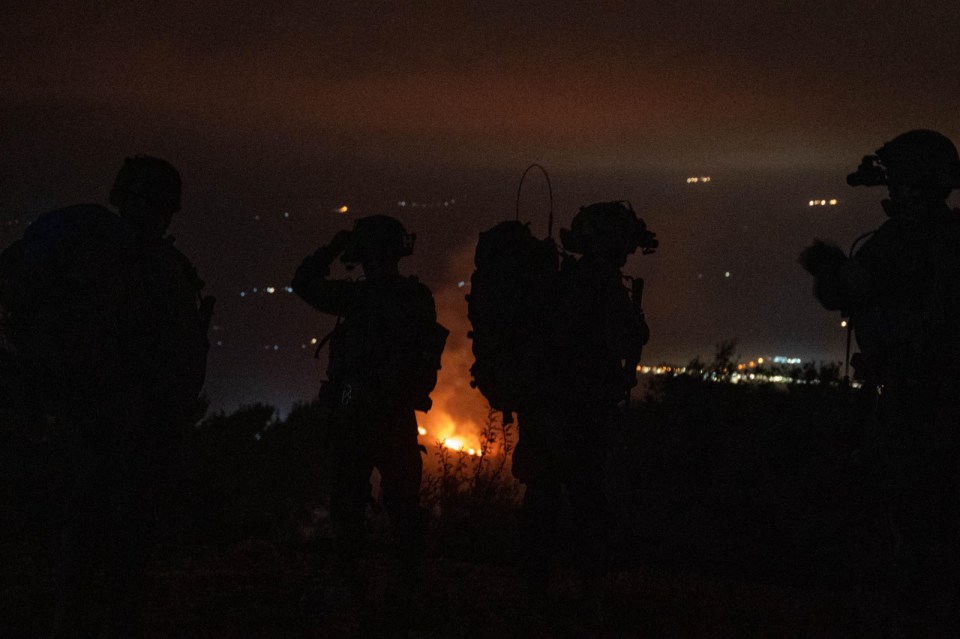 a group of soldiers standing in front of a fire at night