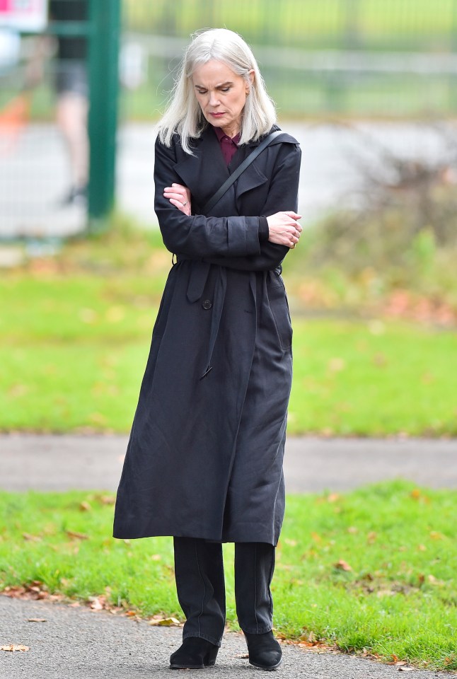 a woman with gray hair wearing a black trench coat