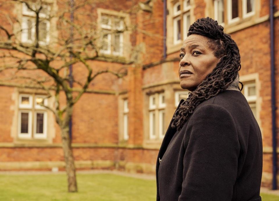 a woman with dreadlocks stands in front of a brick building