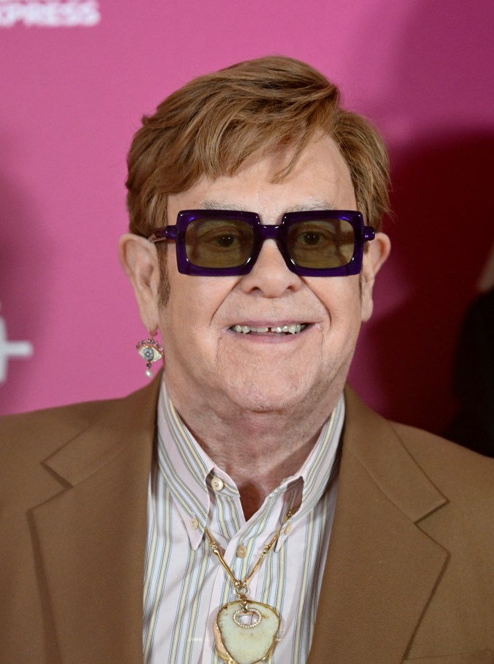 a man wearing sunglasses and a necklace smiles for the camera