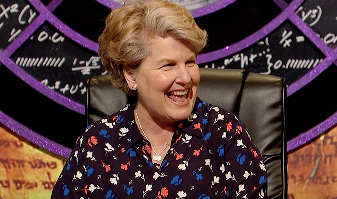 a woman in a floral shirt is smiling in front of a chalkboard with math equations on it