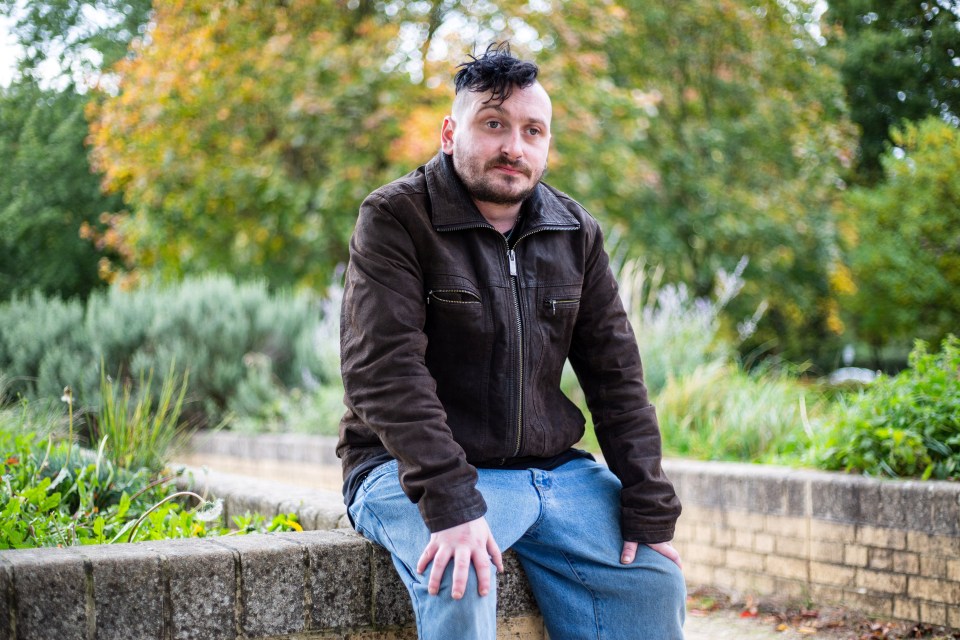 a man in a brown jacket sits on a brick wall