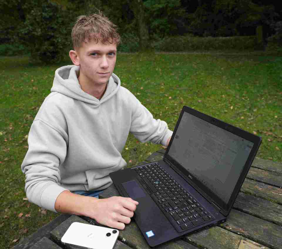 a young man sits at a picnic table using a dell laptop