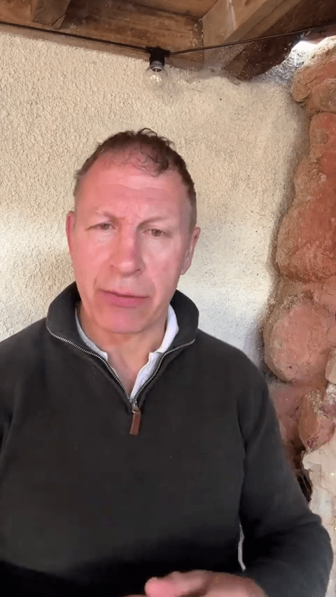 a man in a black sweater stands in front of a stone wall