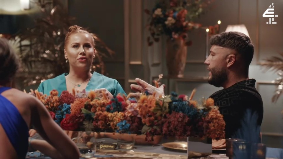 a woman in a blue dress sits at a table with flowers and a man with a beard