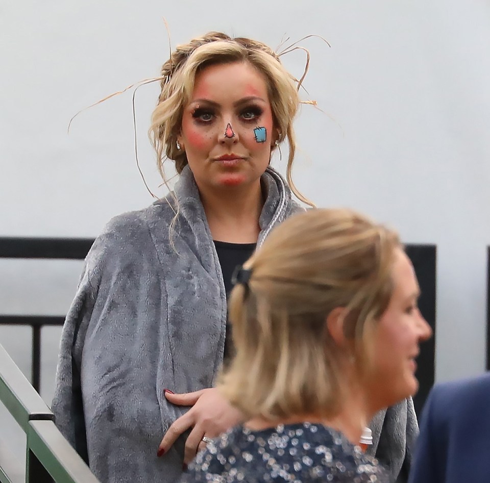 a woman wearing a gray blanket has a blue square painted on her nose