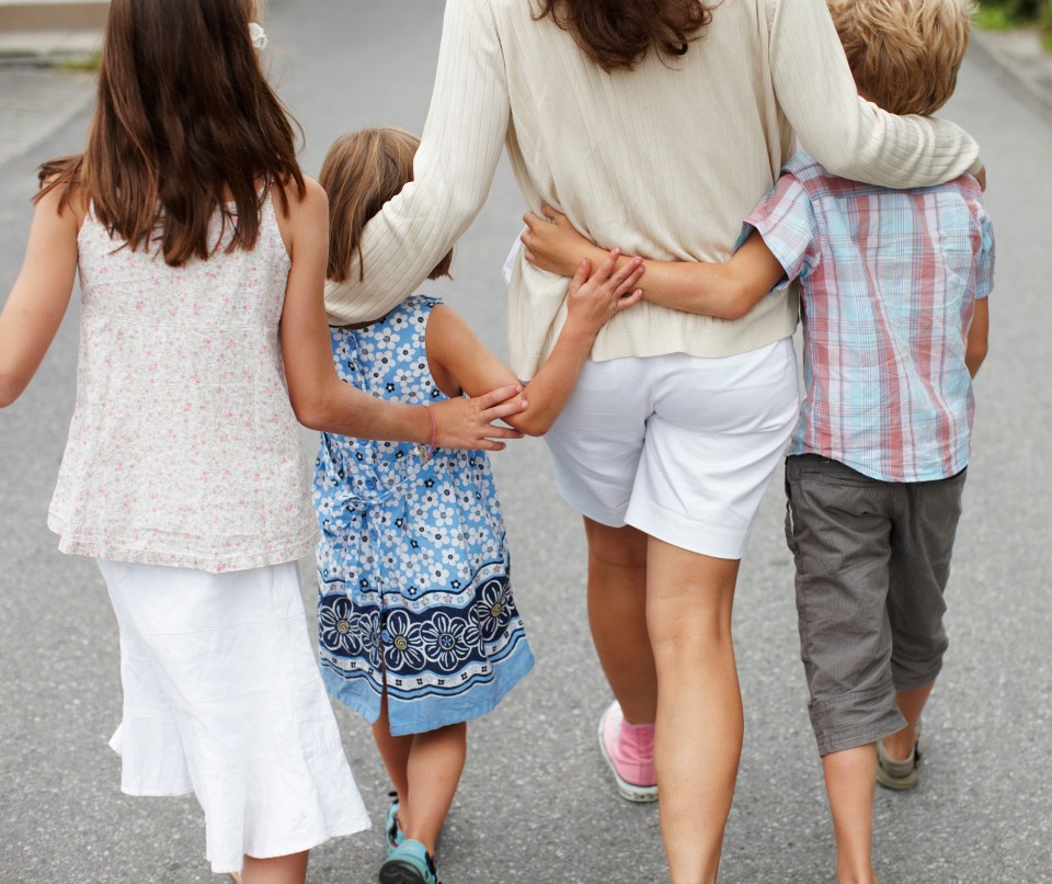 a woman and three children are walking down the street with their arms around each other