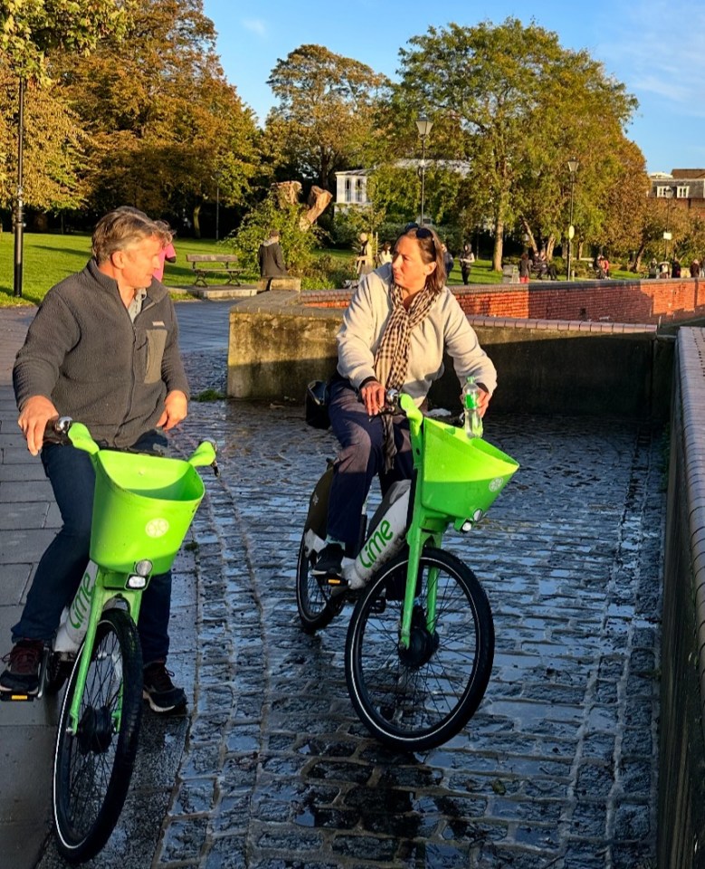 a man and a woman ride lime bikes on a cobblestone street