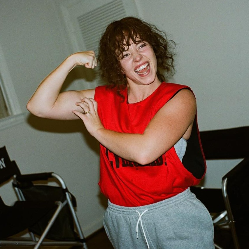 a woman flexes her muscles in front of a christy martin chair