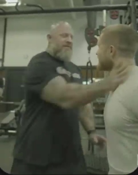 a man with a beard is holding another man 's neck in a gym .