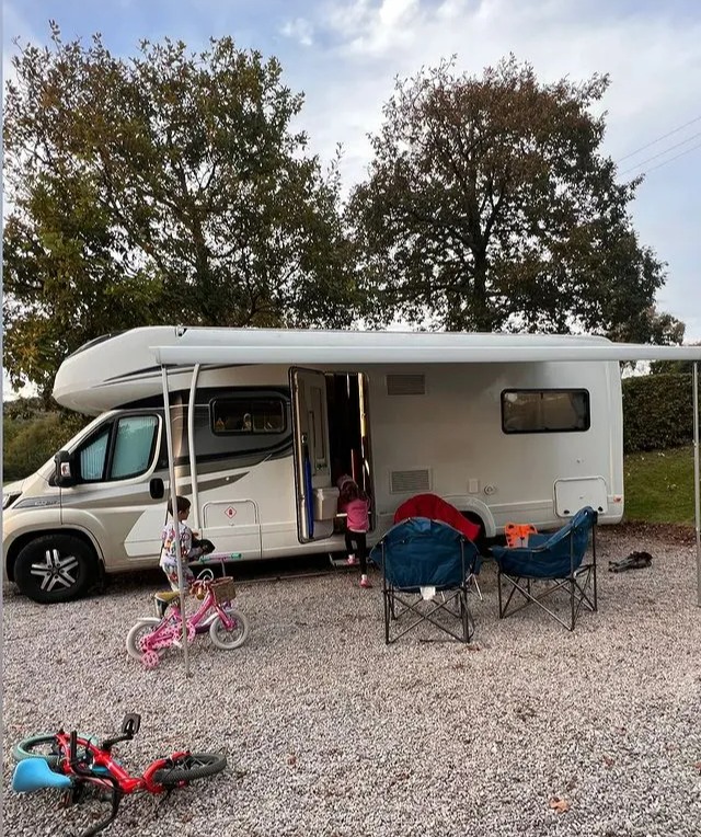 a rv is parked in a gravel area with bikes and chairs