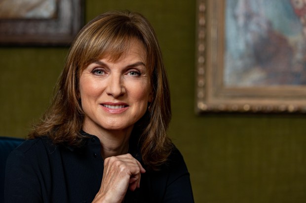 a woman with her hand on her chin smiles in front of a painting