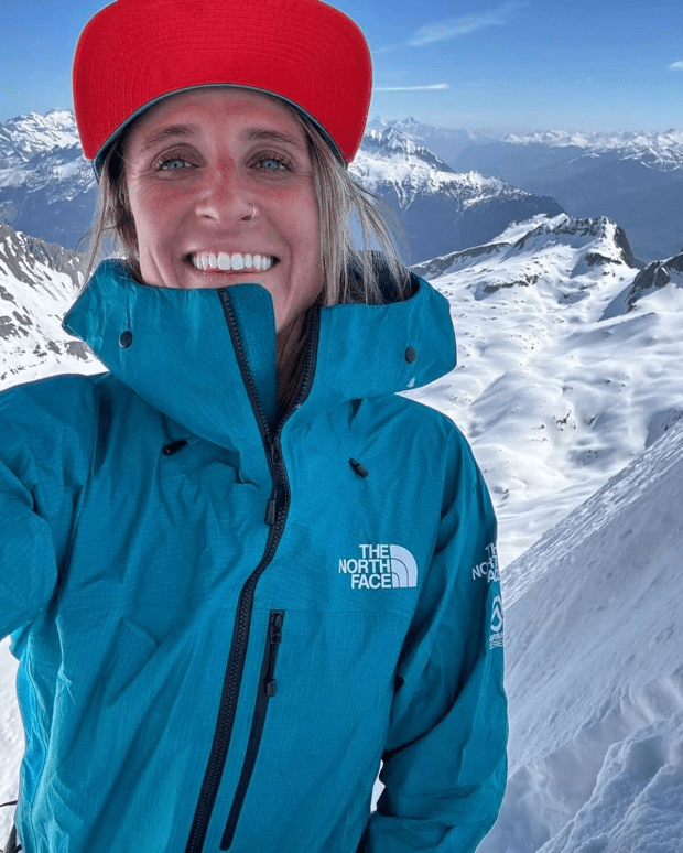 a woman wearing a blue north face jacket smiles in front of a snowy mountain