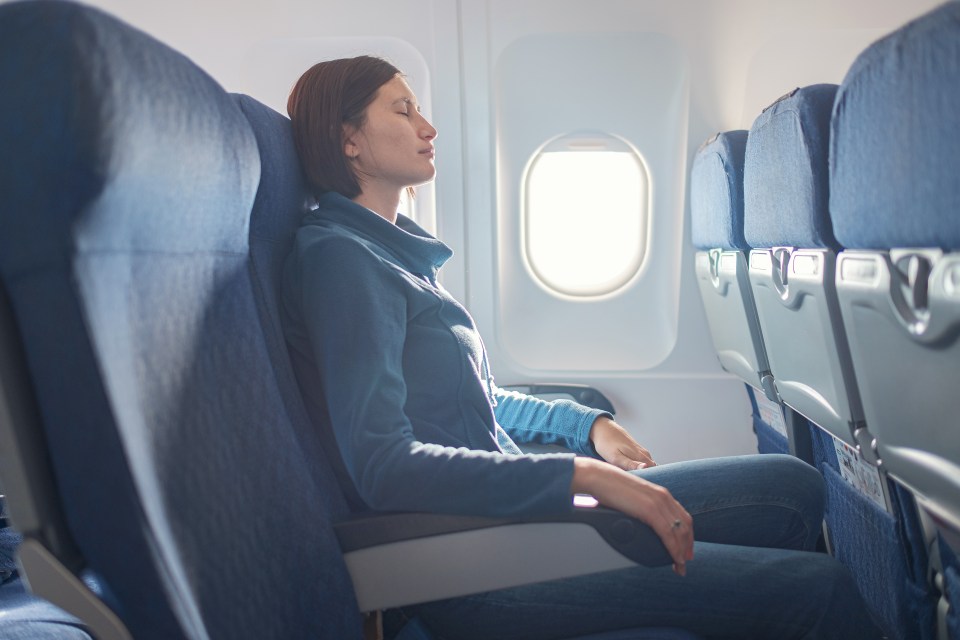 a woman sits on an airplane with her eyes closed