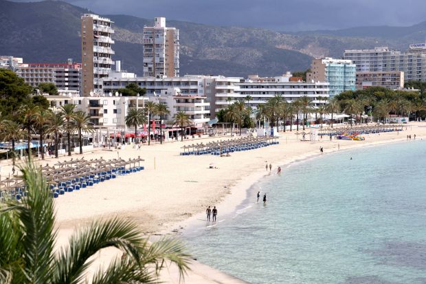 people walking on a beach with a hotel in the background