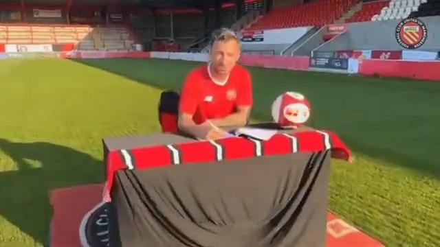 a man is sitting at a table on a soccer field signing a contract .