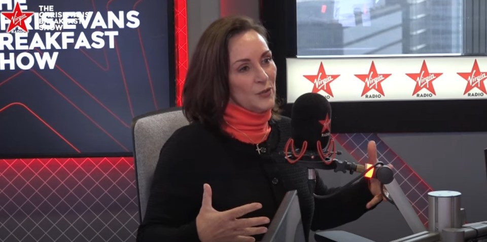 a woman speaking into a microphone in front of a virgin radio sign