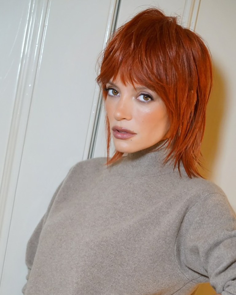 a woman with red hair is wearing a grey sweater