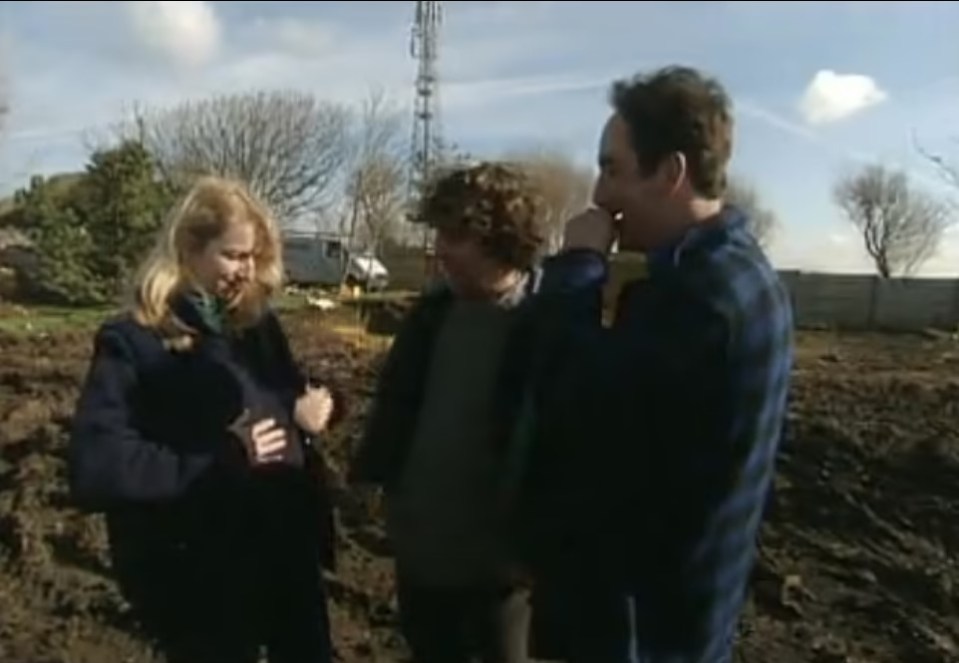 a group of people are standing in a dirt field talking to each other .