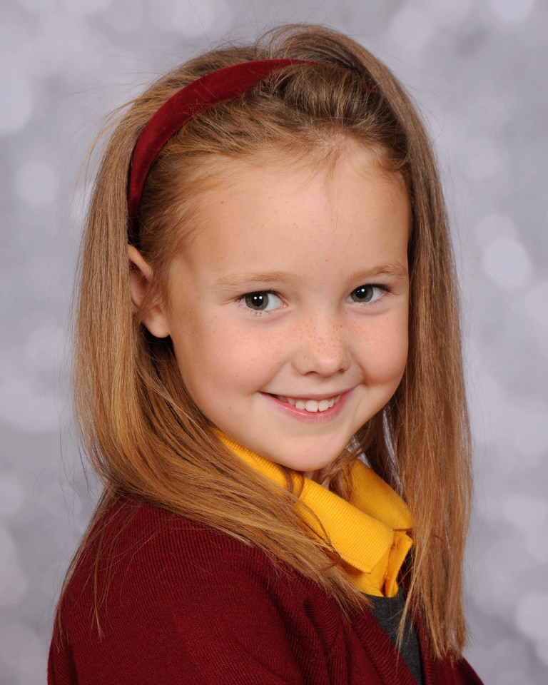 a little girl wearing a red headband and a yellow shirt smiles for the camera