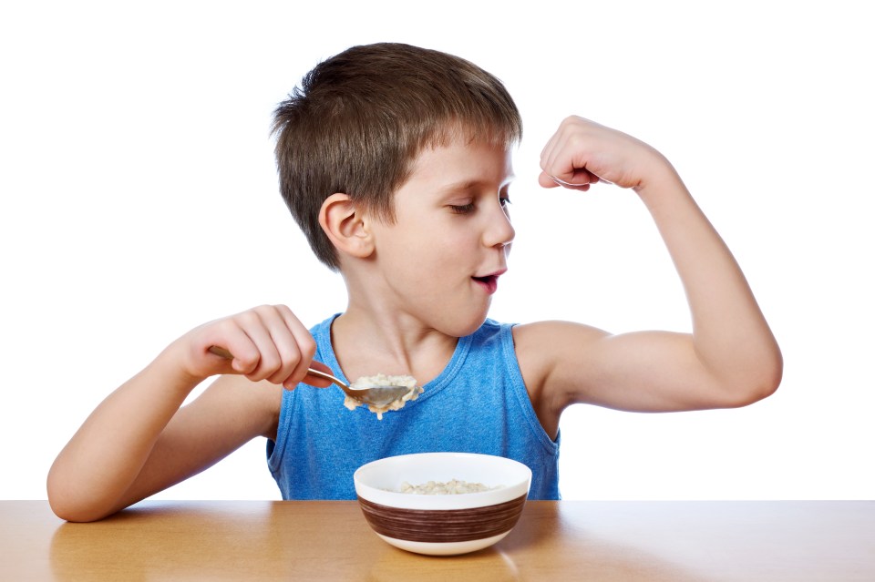 a young boy flexes his muscles while eating cereal from a bowl