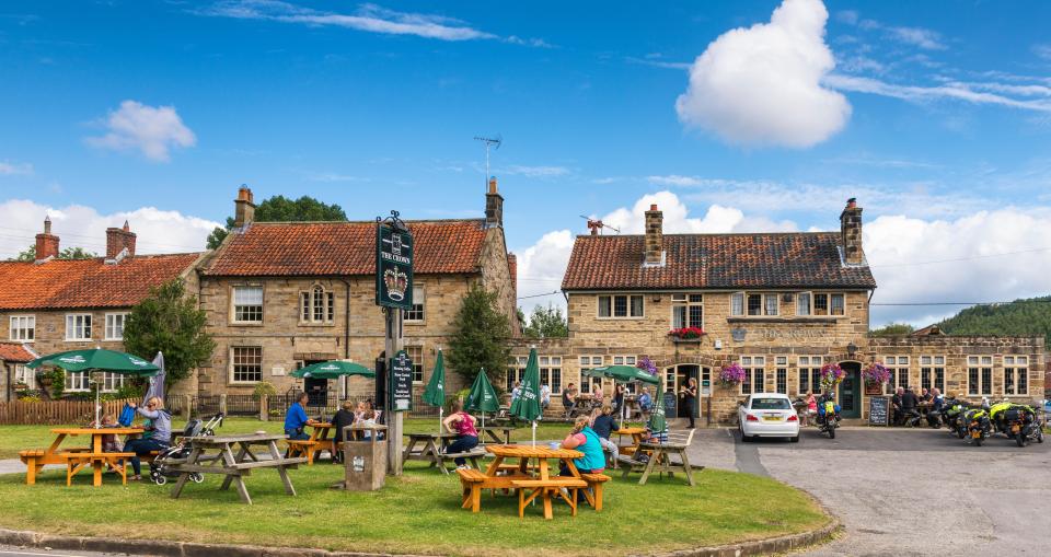 a group of people sit at picnic tables outside a pub