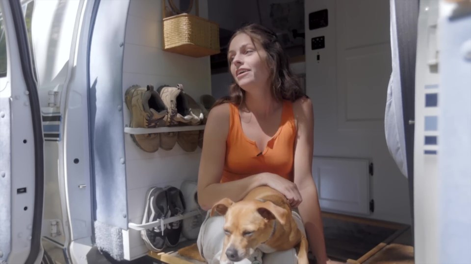 a woman sits in the back of a van with her dog