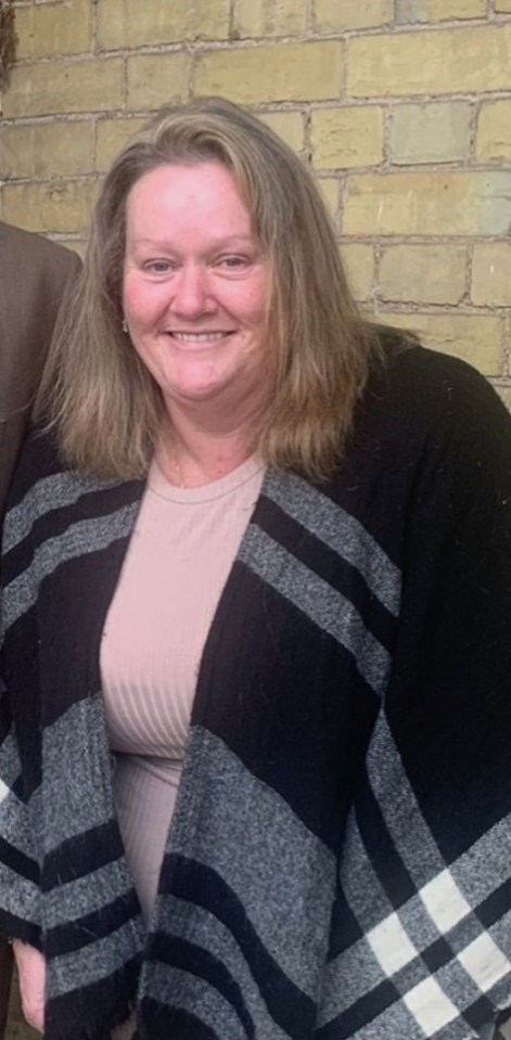 a woman wearing a black and gray plaid sweater smiles in front of a brick wall