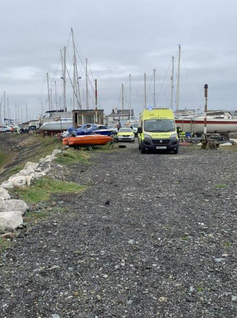 a yellow ambulance is parked in a gravel lot next to boats .