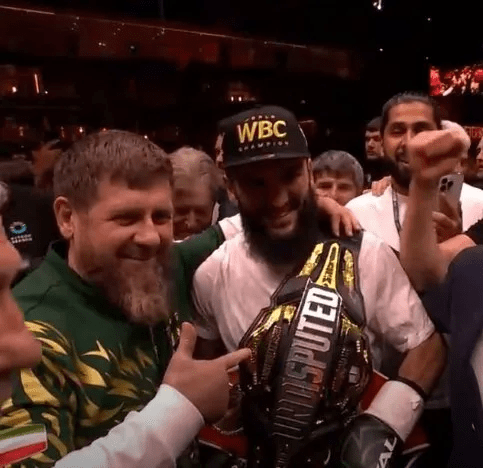 a man with a beard is holding a boxing belt in a crowd of people .